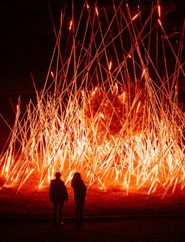 Two people look at a light installation at night - the artwork resembles a bonfire.