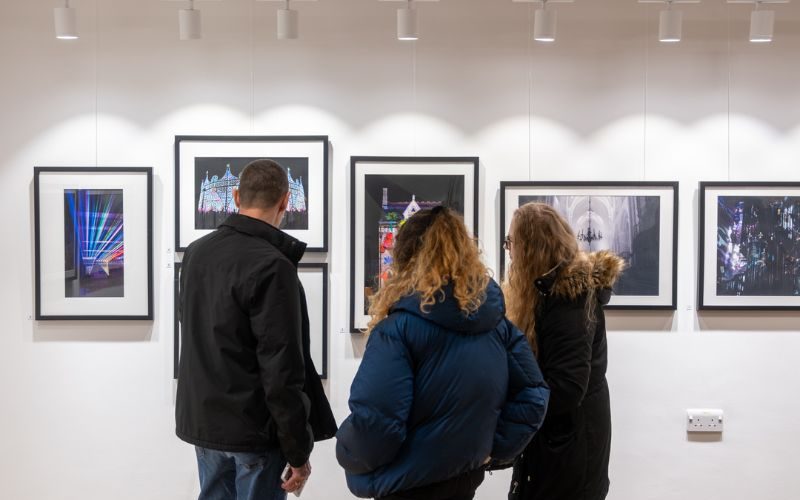 People gather in an exhibition space, looking at framed photographs.